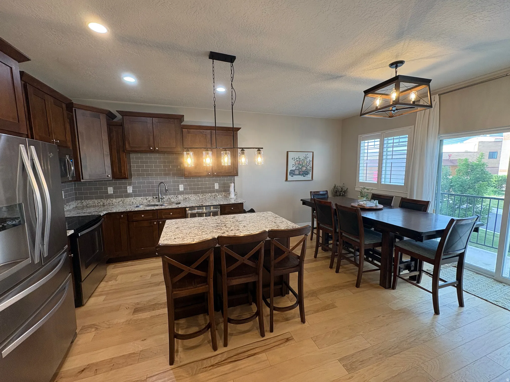 Open-concept kitchen and dining area featuring wood-finish flooring, recessed lighting, and a kitchen island with stone countertop