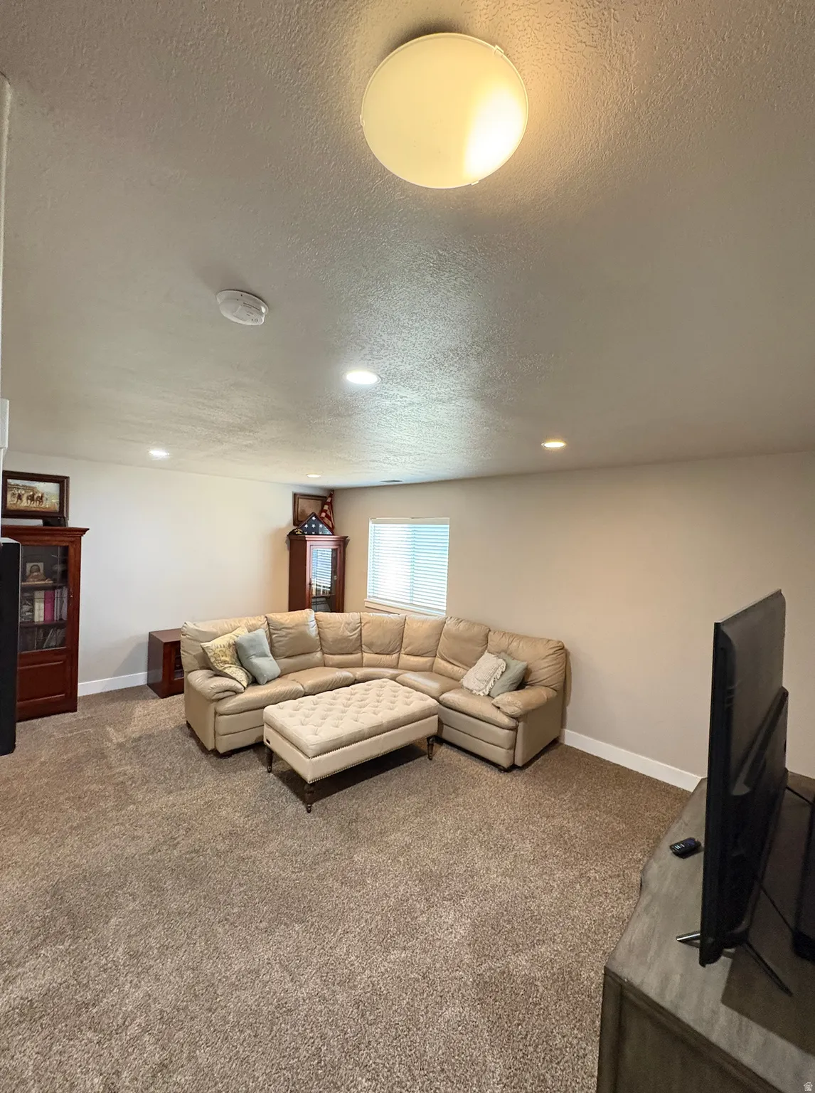 Carpeted room featuring a ceiling-mounted light fixture, recessed lighting, and a white-framed window with horizontal blinds