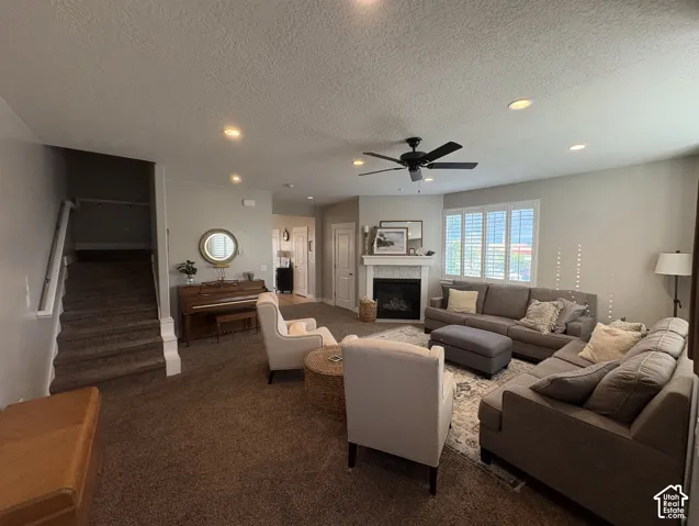 Spacious living area featuring neutral carpeting, recessed lighting, a ceiling fan, and a fireplace with a stone surround and white mantel