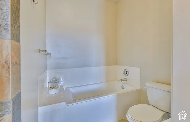 Bathtub with subway tile surround, polished chrome fixtures, and adjacent commode