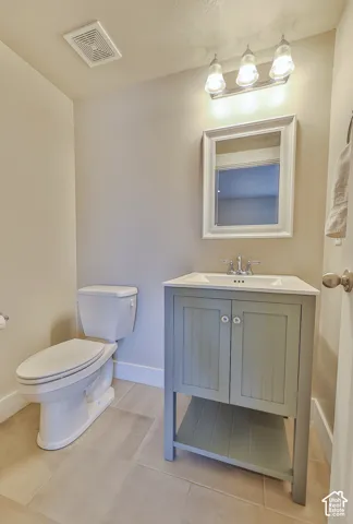 Bathroom featuring a sage green vanity with white ceramic top, rectangular framed mirror, three-light vanity fixture, and large format floor tiles