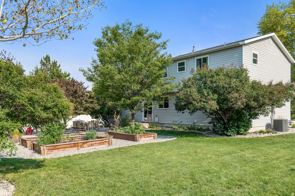 Spacious backyard featuring a manicured lawn, established trees, a gravel patio area with outdoor seating, and multiple raised garden beds