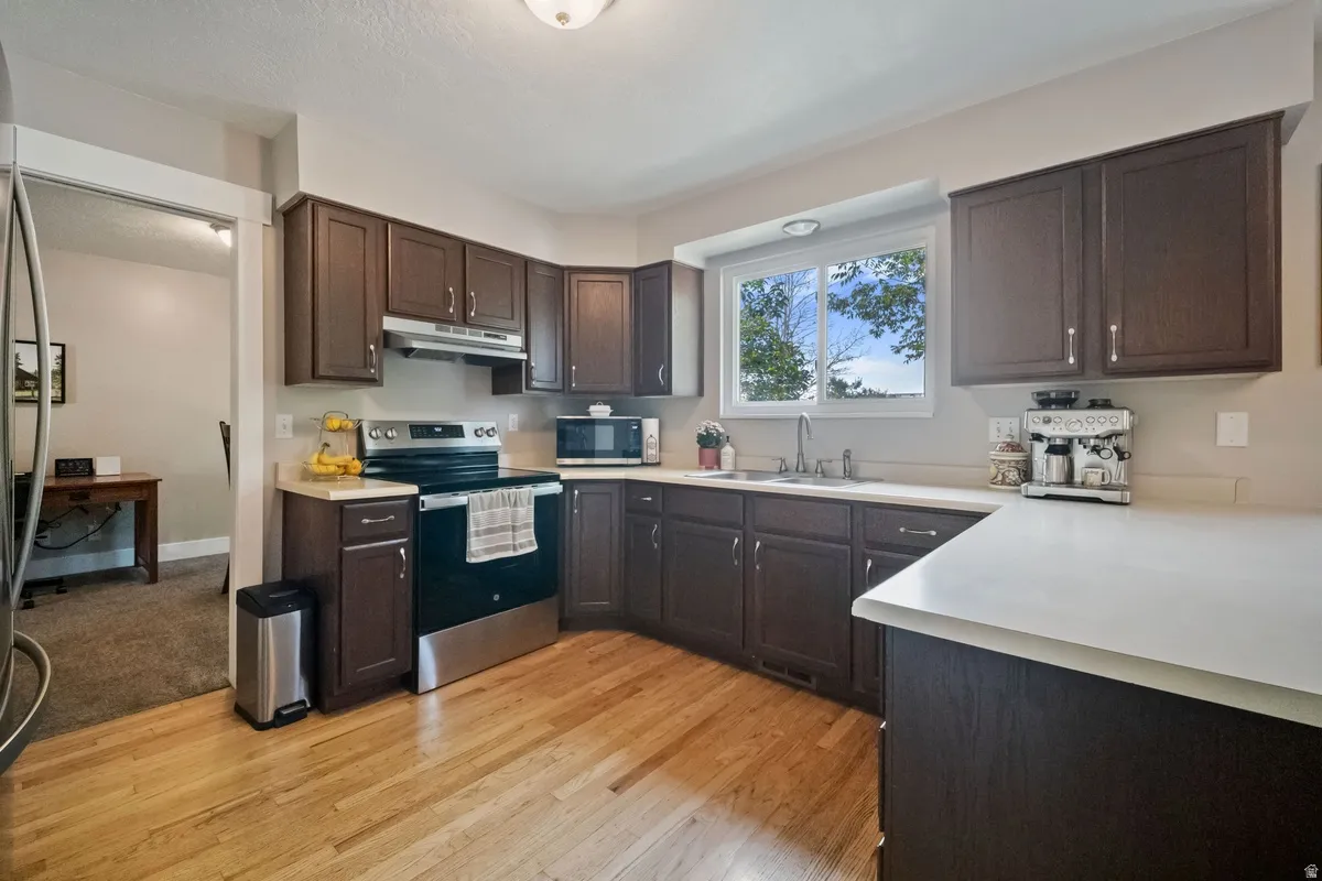 Kitchen featuring wood-finish flooring, dark wood cabinetry, light-toned countertops, and a stainless steel range with overhead microwave
