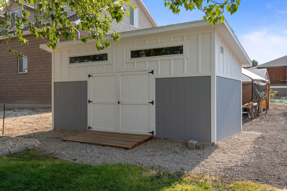 Modern shed featuring two-tone siding, transom windows, double barn doors with black hardware, and a gravel base
