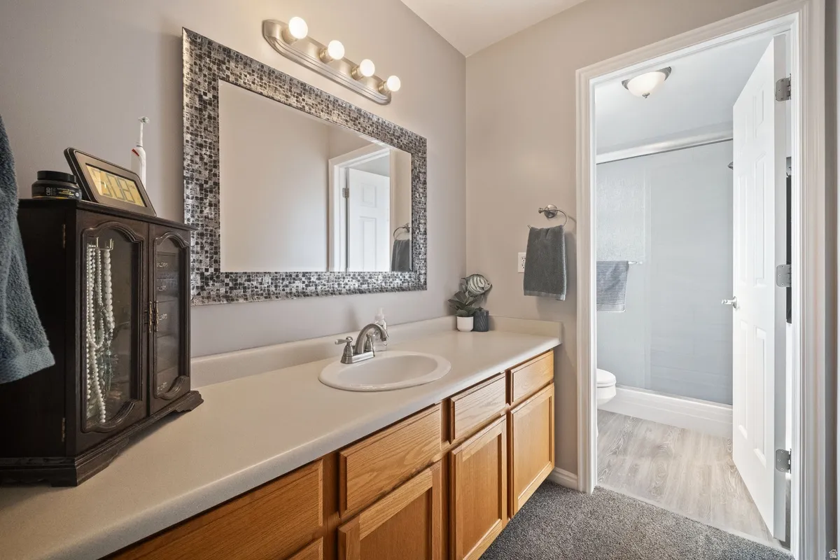Bathroom vanity featuring a mosaic-framed mirror, four-light vanity fixture, single basin sink, and wood-finish cabinetry