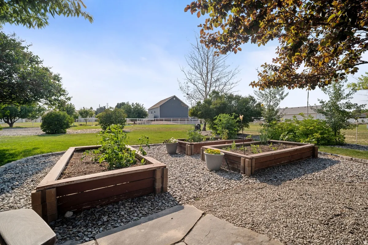 Outdoor garden area featuring multiple wood-finish raised garden beds, a gravel-covered ground, and mature trees