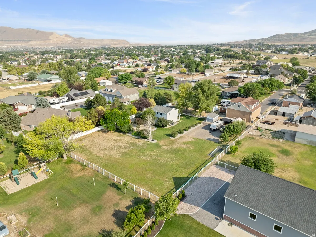 Expansive property featuring a large green space, white fencing, mature trees, a play structure, and a gravel driveway