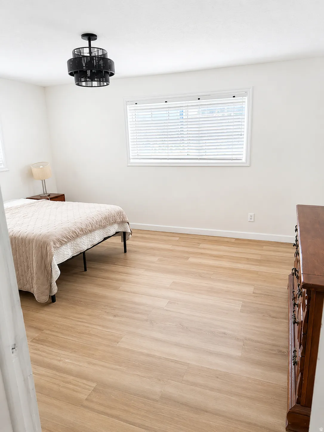 Wood-finish flooring, white walls, and a multi-tiered ceiling light fixture