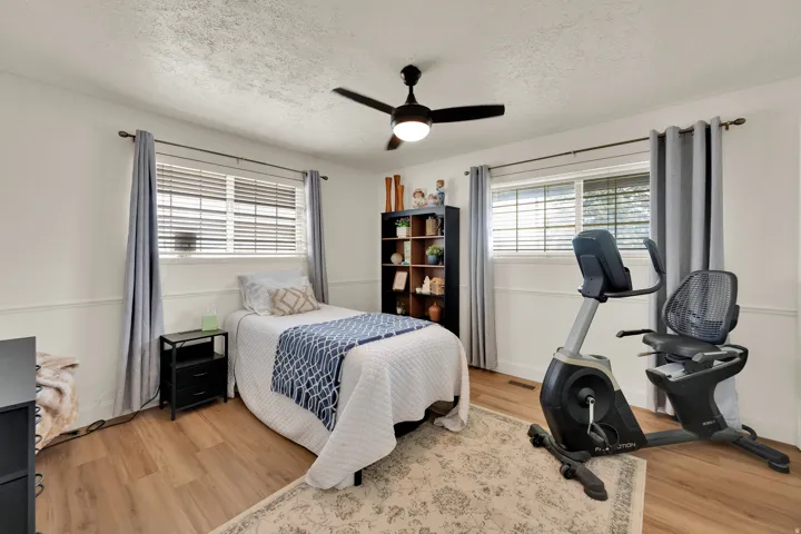 Bright room featuring two large windows with blinds, wood-finish flooring, and a ceiling fan