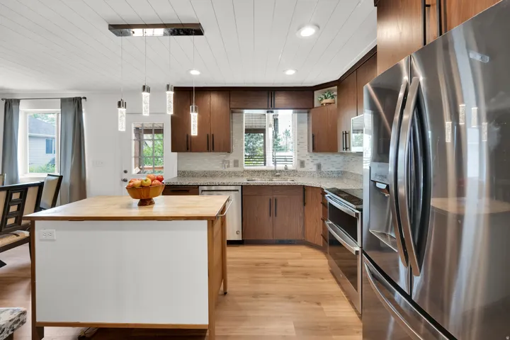 Kitchen featuring wood-finish flooring, shaker-style cabinetry, stainless steel appliances, and a central island with a wood countertop