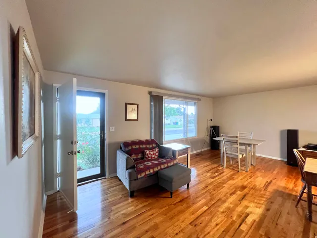 Hardwood flooring extends throughout this expansive living area, featuring a front entry door with a glass panel, a large window providing ample natural light, and neutral wall tones