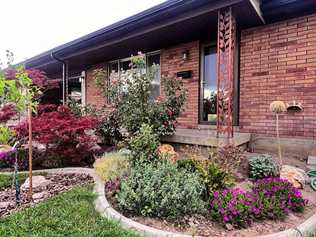 Brick exterior with a decorative metal column, concrete entry, and established landscaping featuring various plantings and a Japanese maple