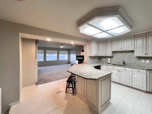 Kitchen featuring an angled breakfast bar with stone countertop, white cabinetry with silver hardware, recessed sink with a chrome faucet, and a mosaic tile backsplash