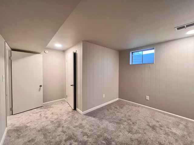 Room featuring light grey vertical paneling, plush grey carpet, and a horizontal window