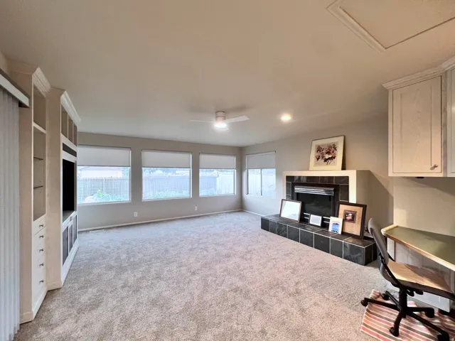 Spacious room featuring a built-in entertainment center, a fireplace with a tiled hearth and surround, a bank of four windows, a ceiling fan, and recessed lighting