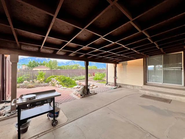 Covered patio featuring an exposed rafter ceiling, concrete flooring, and a sliding glass door