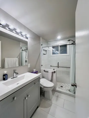 Contemporary bathroom featuring a grey vanity with an integrated white sink, a frameless glass shower enclosure, a pebbled shower floor, white subway tile shower walls, and large format rectangular floor tiles