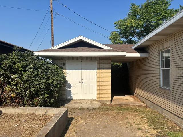 Brick and siding exterior with attached garage featuring double doors and carport structure