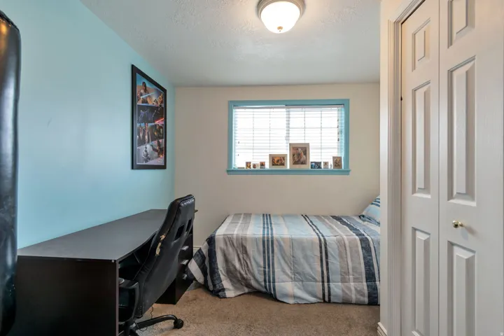 Bedroom featuring light blue accent wall, neutral carpeting, and a window with horizontal blinds