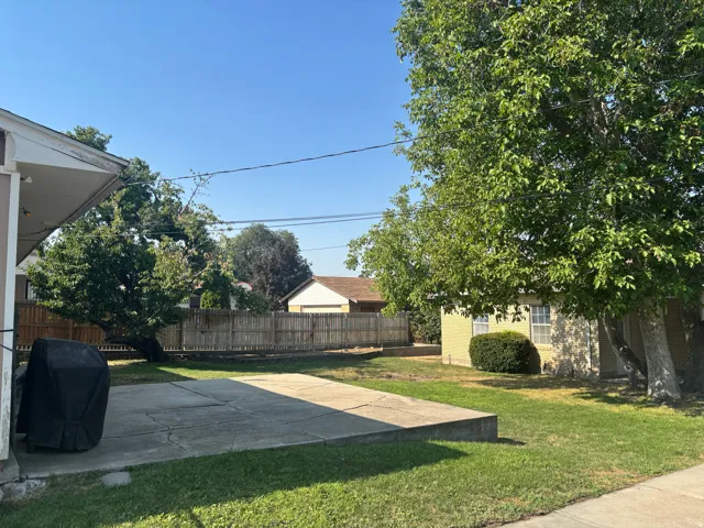 Spacious backyard retreat featuring mature shade trees, level lawn, and wooden perimeter fencing