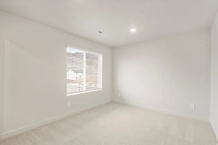 Neutral-toned room featuring a large window with blinds, recessed ceiling lighting, and light carpeting