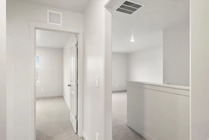 Interior hallway featuring light gray wall paint, white trim, and light gray carpet flooring