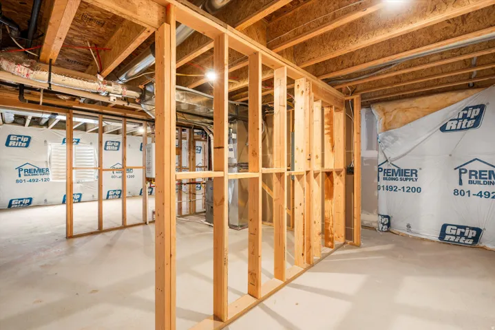Unfinished basement space featuring visible wood framing, concrete flooring, exposed ceiling joists, and a window opening