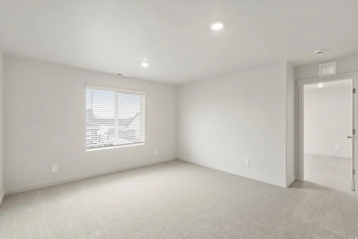 Spacious room featuring neutral paint, recessed lighting, a large window with blinds, light-colored carpet, and an open doorway