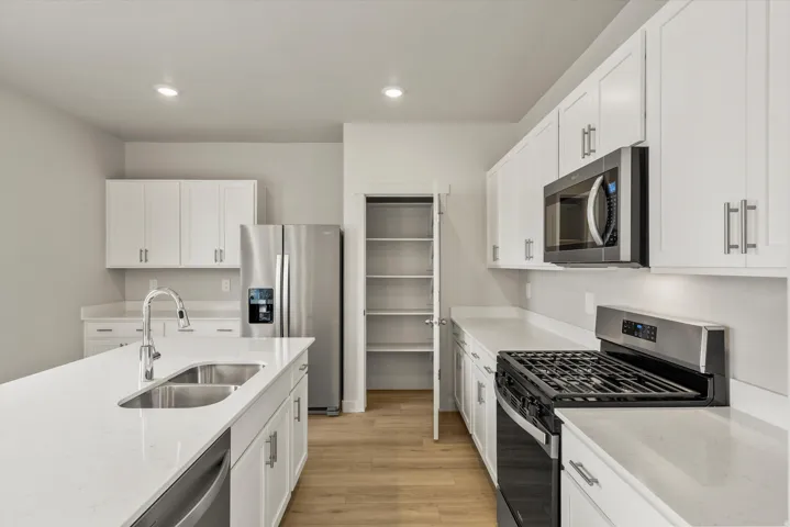 Modern kitchen featuring white cabinetry, light-toned countertops, stainless steel appliances, a center island with an undermount sink, and wood-finish flooring