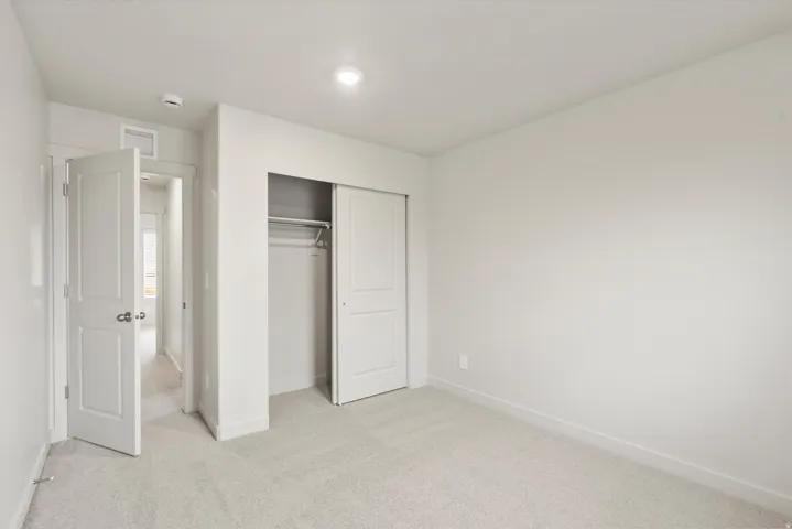 White-painted interior room featuring light-colored carpet flooring, a closet with sliding panel doors, and a recessed ceiling light fixture