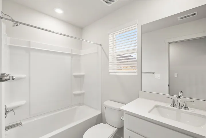 White bathroom featuring a shower-over-tub combination with a built-in shelving system, a single vanity with an undermount sink, a stone-finish countertop, and a chrome faucet