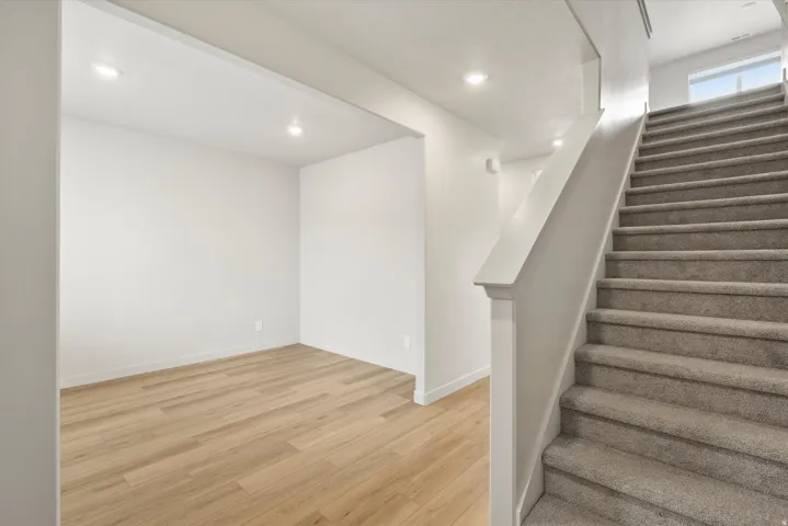 Carpeted staircase with white railing, recessed lighting, and a window providing natural light at the landing