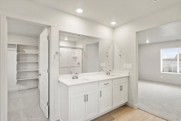 Dual vanity with white cabinetry and integrated sinks, a large wall-mounted mirror, and recessed lighting