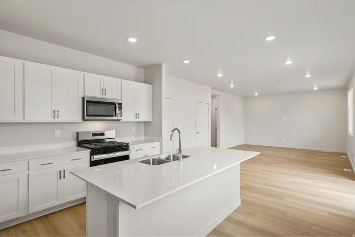 Bright kitchen featuring an island with a double basin sink, white cabinetry, stainless steel appliances, white countertops, and wood-finish flooring