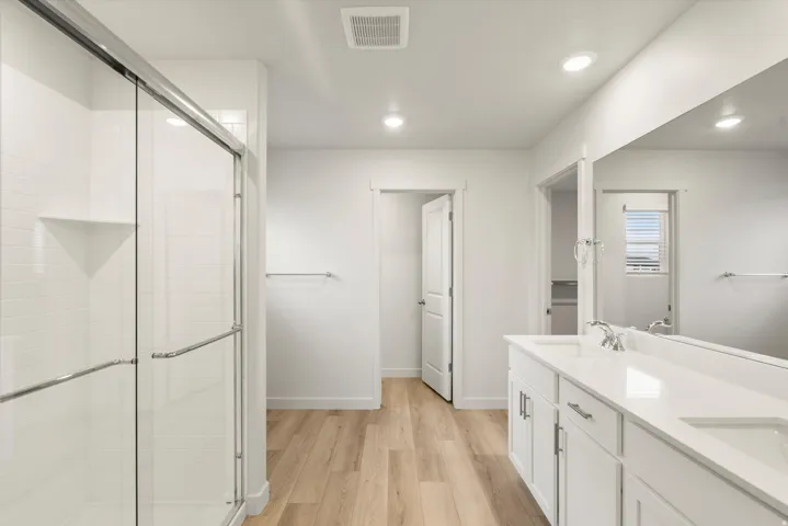 Bathroom featuring a dual vanity with white cabinetry and integrated sinks, a large mirror, and recessed lighting