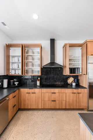 Contemporary kitchen featuring warm wood-finish cabinetry, dark countertops, and a full-height black tile backsplash