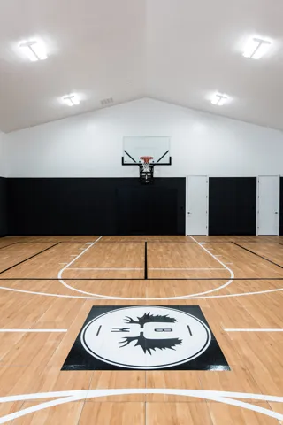 Indoor basketball court featuring wood-finish flooring with court markings, a mounted hoop, and a custom floor logo