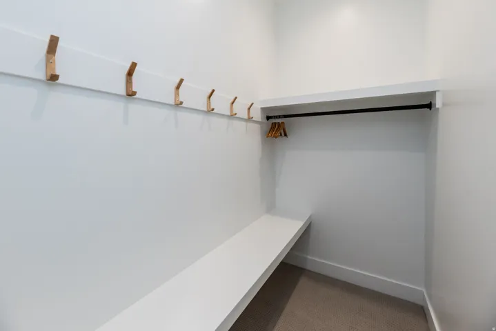 Entryway mudroom featuring a built-in bench, seven wall-mounted hooks, overhead shelving, and a garment rod