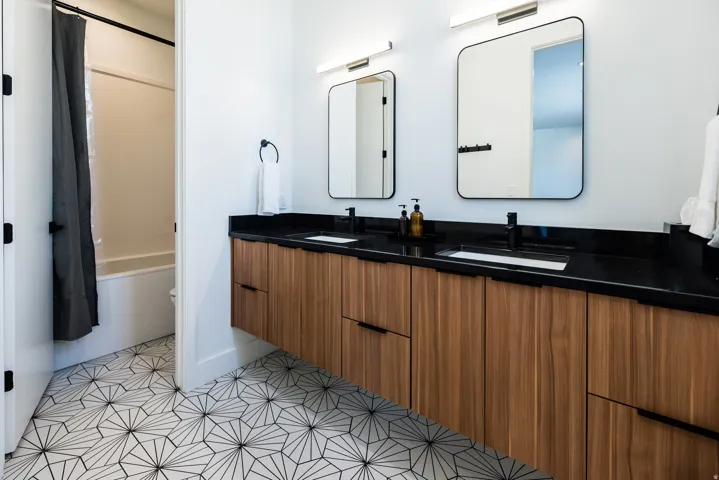Contemporary bathroom featuring a floating wood-finish double vanity with a dark countertop and integrated sinks