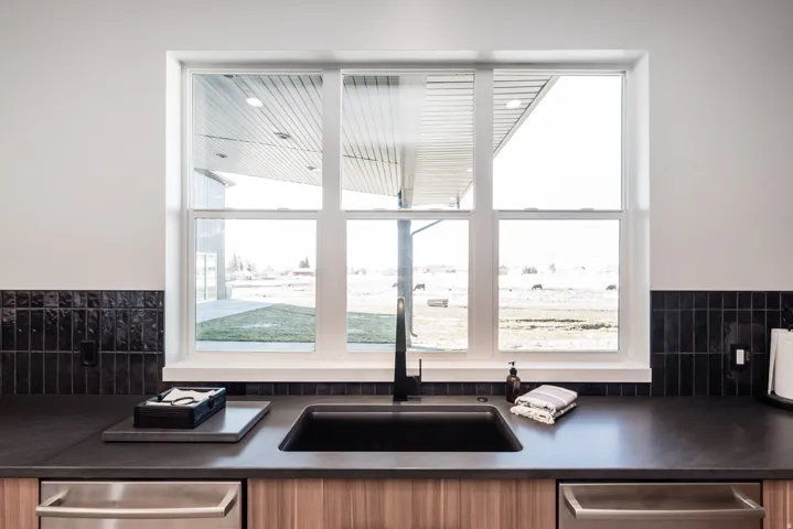 Kitchen features a triple-pane window, dark solid surface countertops, a black undermount sink with a matte black faucet, and a black subway tile backsplash