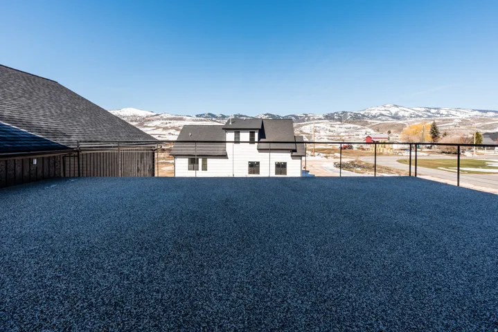 Spacious rooftop deck featuring a dark gray textured surface, black metal railings, and clear glass balusters