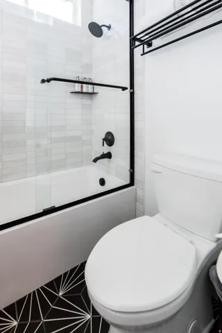 Bathroom featuring a shower-tub combination with black-framed glass enclosure, matte black fixtures, white subway tile surround, and a geometric pattern floor tile