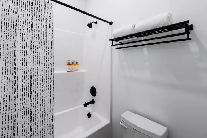Full white bathtub with black fixtures, including a shower head, faucet, and shower rod