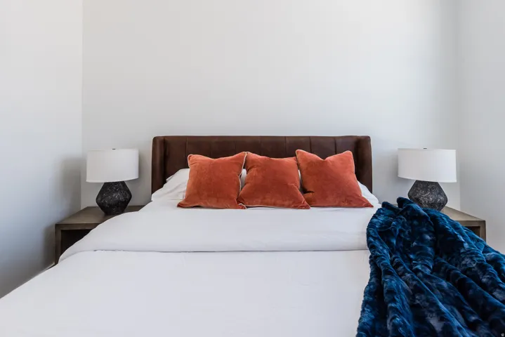 Bedroom featuring a leather upholstered headboard, clean white walls, and two integrated bedside tables with lamps