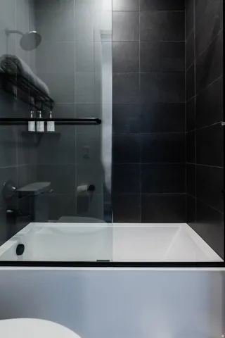 Contemporary bathtub and shower combination featuring dark tile surround