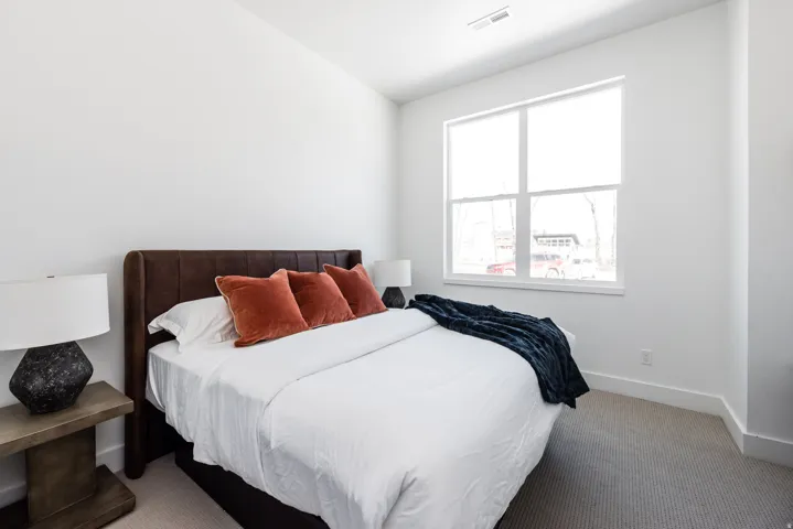 Bright bedroom featuring a large window, neutral wall paint, and gray carpet flooring