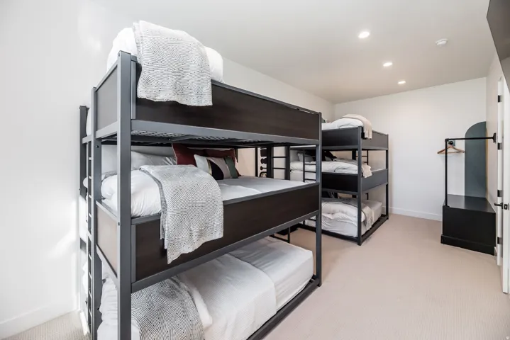 Room featuring multiple bunk beds with dark frames and white bedding, recessed ceiling lighting, light-colored carpet, and a built-in wardrobe with an arched accent