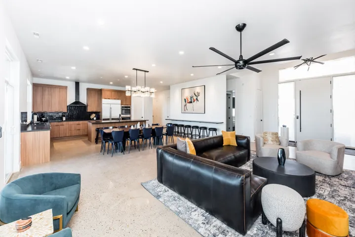 Open-concept living area featuring light-toned flooring, a kitchen with wood-finish cabinetry, a large dining island, and a contemporary black ceiling fan