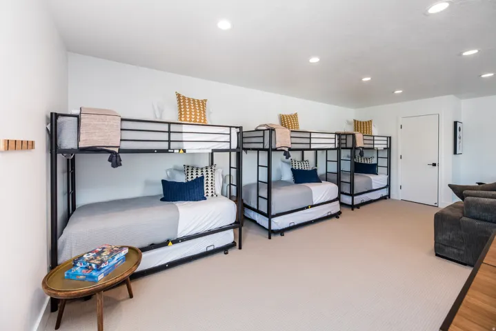Spacious room featuring three metal-frame bunk beds with trundles, white walls, recessed lighting, and light-colored carpet flooring