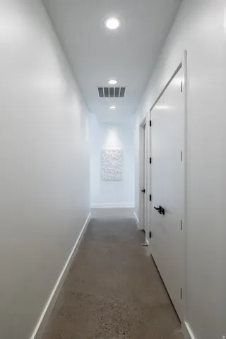 Modern interior corridor featuring recessed ceiling lighting, a white painted finish, and a textured wall art piece